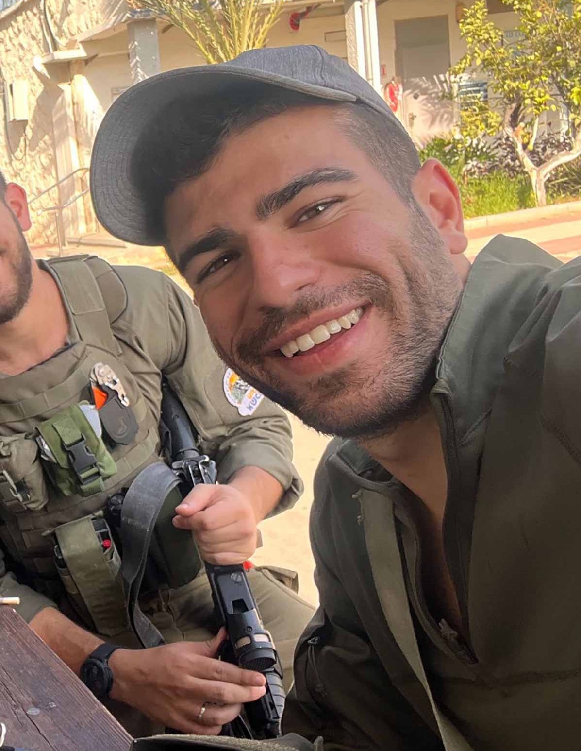 הוד גויטע במילואים, זיפי זקנקן ושפם, עם כובע יושב עם חבר ומחייך