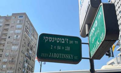 שלט רחוב בפינת רחוב ז'בוטינסקי 2 וביאליק 1, ברקע בצד ימין ושמאל בניינים גבוהים