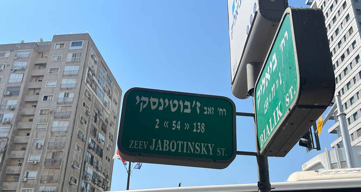 שלט רחוב בפינת רחוב ז'בוטינסקי 2 וביאליק 1, ברקע בצד ימין ושמאל בניינים גבוהים