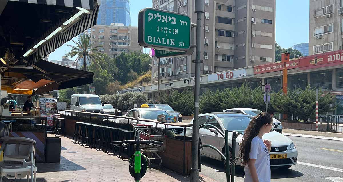 רחוב ז'בוטינסקי פינת ביאליק, מכוניות עוצרות לפני מעבר חצייה להולכת רגל בחולצה לבנה