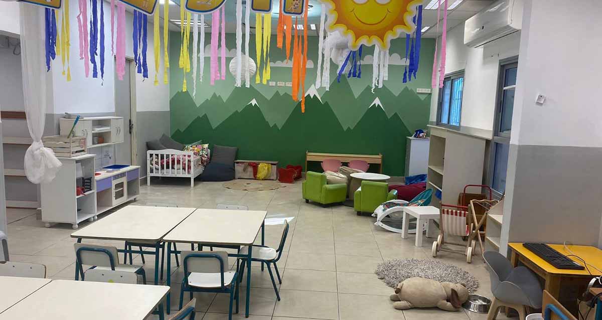 רהיטים חדשים בכיתה, שולחנות וכסאות לבנים, פינת ישיבה, לול לילד קטן, דובי וקישוטים בתקרה