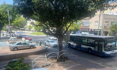רחוב הרא"ה ברמת גן, אוטובוס דן בכביש ובשני המסלולים מכוניות פרטיות. במדרכה באמצע התמונה עץ גדול ובצד שמאל חניון למכוניות פרטיות. ברקע בתי מגורים ועצים במדרכות
