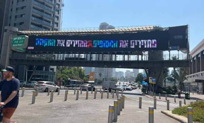 שלט ענק תלוי על גשר הולכי רגל מעל רחוב שלום זיסמן. בשלט כתוב: מחזירם את החטופים מחזירים את התקווה