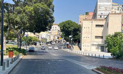 שדרה עם 2 נתיבים בכל כיוון, בניין הרבנות והמועצה הדתית בצד ימין, וגינה עם כסאות בצד שמאל תחת עץ גדול