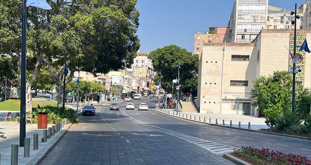שדרה עם 2 נתיבים בכל כיוון, בניין הרבנות והמועצה הדתית בצד ימין, וגינה עם כסאות בצד שמאל תחת עץ גדול