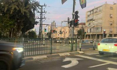 צומת הרחובות ביאליק ואבא הלל עם רמזורים לרכב ולהולכי רגל. רחוב אבא הלל בן שני מסלולים ופס צר של שטח מרוצף עם גדר מתכת מפרידים בין המסלולים. בצד ימין של רחוב ביאליק בניין מגורים בן 4 קומות. ומשמאלו בנייני מגורים של שלוש קומות. בצד שמאל באבא הלל עץ גבוה ורחב ולימינו עמוד חשמל של מתח גבוה.