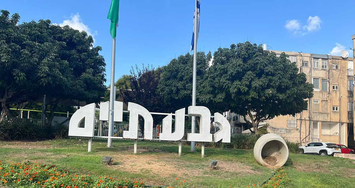 הכניסה לגבעתיים מדרך השלום. שלט בן שני חלקים בצורת גבעות, בגבעה מימין שלוש אותיות: גבע, ובגבעה משמאל ארבע אותיות: תיים. מאחורי השלט שני תרנים עם דגל המדינה ודגל העיר. השלט מוצב על משטח דשא. מאחורי השלט עצים גדולים ורחבים ובצד ימין בניין מגורים בן 4 קומות.