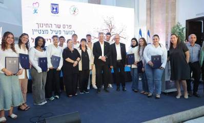 פרס לזכרו של לוחם האש אלעד ריבן ז"ל. צילום קבוצתי של המשתתפים בטקס עם שר החינוך יואב קיש והתלמידה ליאור אליאס תלמידה מרמת גן וזוכים נוספים. ברקע שלט ענק עם סמל המדינה וכיתוב: פרס שר החינוך לנוער פעיל מצטיין לזכרו של אלעד ריבן ז"ל. מימין לכיתוב תמונה של עץ שרוף. דגלי המדינה ברקע.