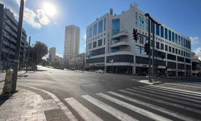 צומת רחוב ז'בוטינסקי ודרך בן גוריון, מעברי חצייה להולכי רגל ורמזורים בארבעת הצדדים של הצומת. בצד ימין בניין םינתי בן 4 קומות ובצד שמאל בניין פינתי בן 7 קומות וחנויות בקומת הקרקע. ברקע בניין גבוה.