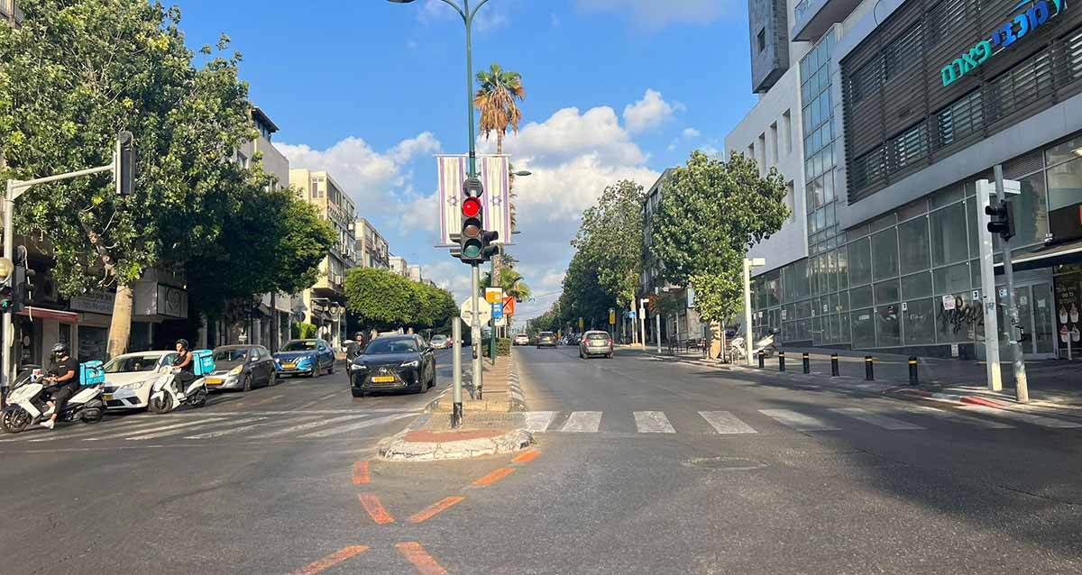 רחוב כצנלסון בגבעתיים, במרכז רמזור של הכניסה לרחוב ולפניו מעבר חצייה להולכי רגל בין שני צידי הרחוב. ברחוב שני מסלולים ושני נתיבים בכל מסלול. מכוניות חונות ומכונית נוסעות בשני המסלולים. בצידי הרחוב בניינים בני שלוש/ארבע קומות ועל המדרכות עצים גדולים.