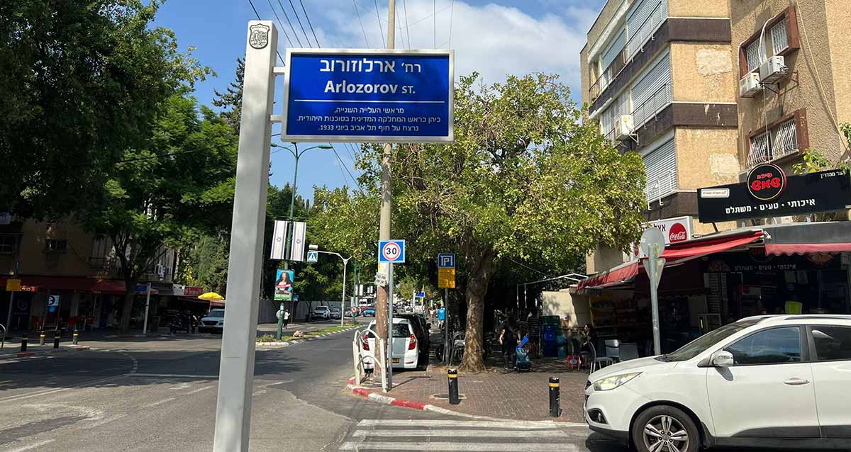 רחוב ארלוזורוב בגבעתיים, שלט רחוב כחול עם כיתוב בלבן. שם הרחוב בעברית ובאנגלית. מתחת לשם הרחוב כיתוב: מראשי העלייה השנייה, כיהן כראש המחלקה המדינית בסוכנות היהודית. נרצח על חוף תל אביב ביוני 1933. בצד ימין בתי מגורים וחנויות בקומת הקרקע. בצד שמאל הרחוב הניצב לארלוזורוב עם עצים גבוהים על המדרכה ומאחוריהם מציצים בניינים.