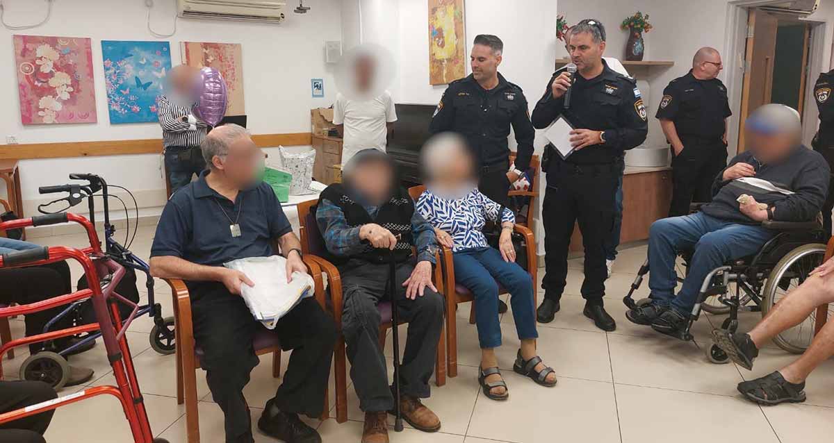 מפקדי ושוטרי תחנת גבעתיים חוגגים 100 לניצול שואה. בן ה-100, אישה לשמאלו ואיש לימינו יושבים על כורסאות ופניהם מוסתרות. מאחוריהם עומדים שני מפקדים, שוטר, ועוד שני אנשים שפניהם מוסתרות. בצד ימין יושב אדם על כסא גלגלים ופניו מוסתרות.