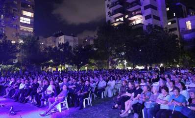 טקס עירוני בגבעתיים לציון 7 באוקטובר. תמונה של הקהל הרב היושב על כסאות פלסטיק לבנים ברחבה עצומה. ברקע בנייני מגורים ועצים.