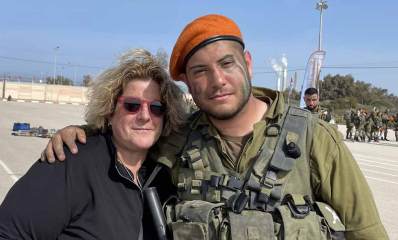עומרי ניב פיירשטין ז"ל במדים עם אמו אור-לי ניב סגנית ראש העיר גבעתיים, עומדים מחובקים במגרש בו נמצאים ברקע חיילים רבים. עומרי חובש כומתה כתומה וחגור על גופו. האם אור-לי מרכיבה משקפי שמש ולבושה בבגד שחור.