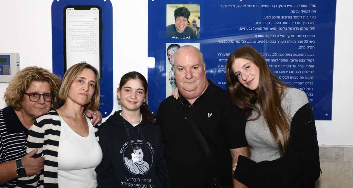 אולם ספורט ע"ש עומרי ניב פיירשטין. תמונה של המשפחה על רקע של שני לוחות כחולים ובהם תמונה של עומרי ותולדות חייו.