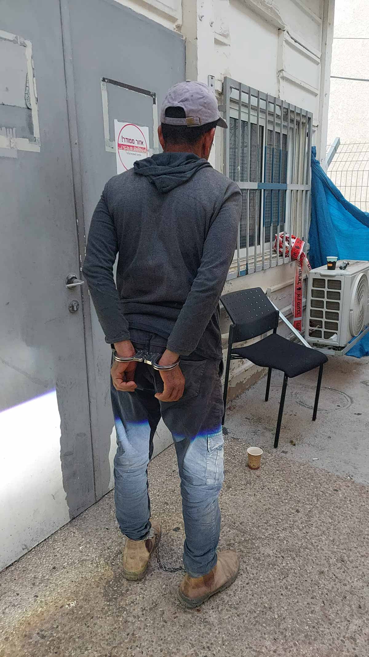 מעצר חשוד שוהה בלתי חוקי. הוא עומד אזוק בידיים וברגליים.