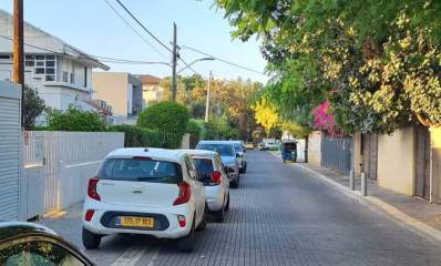 שכונת ותיקים רמת גן. רחוב חד סיטרי עם מדרכה צרה בצד ימין. בצד שמאל חונות מכוניות צמוד לגדרות הבתים וללא מדרכה, במדרכה בצד ימין קלנוע. בחזית הבתים חומות בטון או גדרות קרשים או גדר חי. עם צמחייה. בצד שמאל שורת בתים בני שתי קומות.