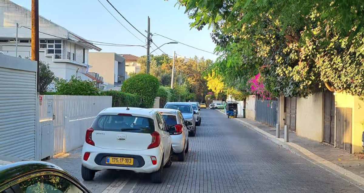 שכונת ותיקים רמת גן. רחוב חד סיטרי עם מדרכה צרה בצד ימין. בצד שמאל חונות מכוניות צמוד לגדרות הבתים וללא מדרכה, במדרכה בצד ימין קלנוע. בחזית הבתים חומות בטון או גדרות קרשים או גדר חי. עם צמחייה. בצד שמאל שורת בתים בני שתי קומות.
