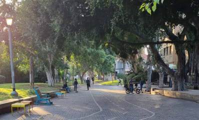 שכונת ותיקים רמת גן. רחוב להולכי רגל בלבד עם ספסל וכסאות ישיבה צבעוניים. בצד ימין בתי מגורים ובצד שמאל פארק, עם דשא וצמחייה רבה. במדרחוב הולכים אנשים ורוכב אופניים אחד.