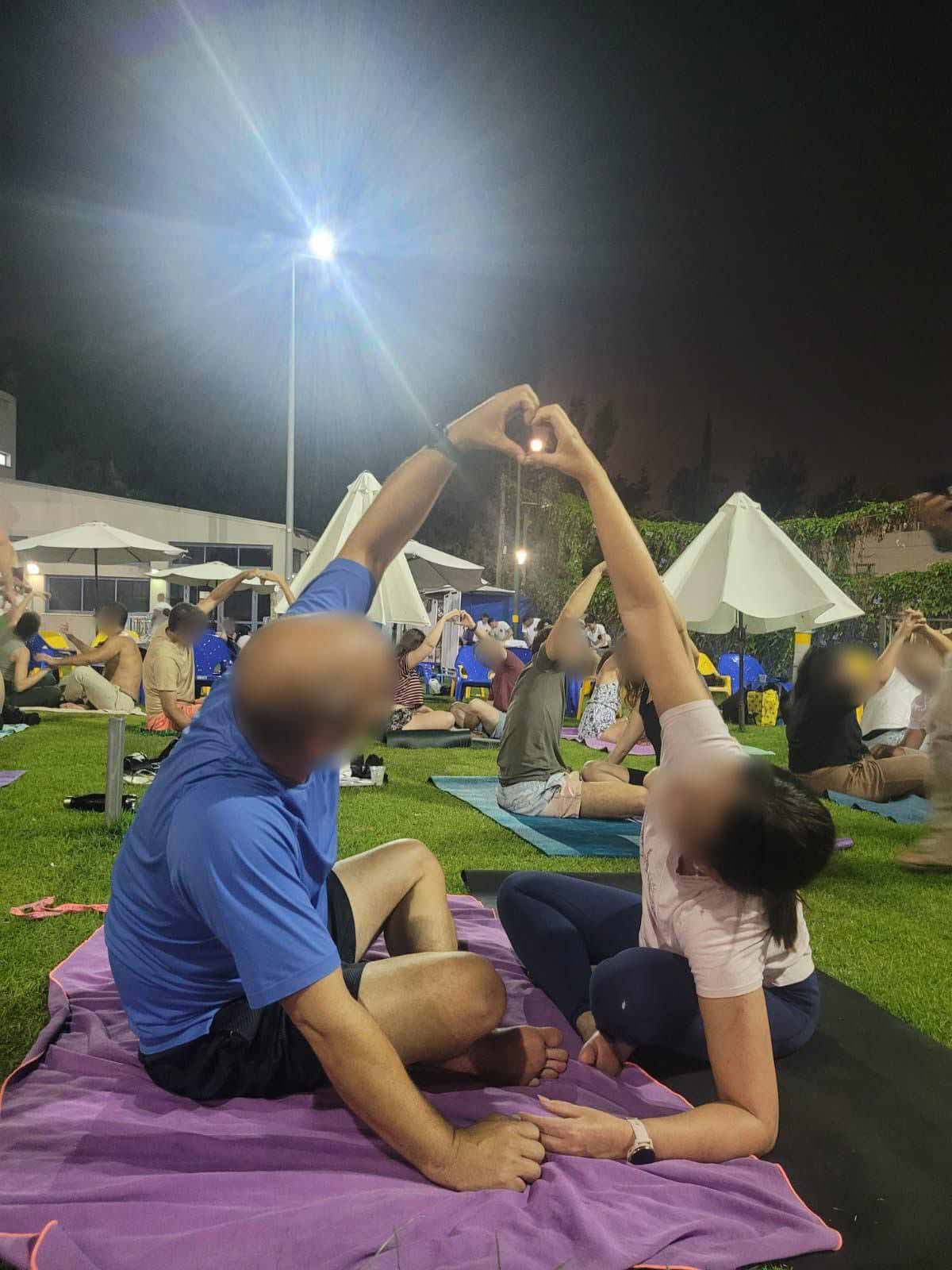 שבוע הוקרה לפצועי צה"ל ברמת גן. על רחבה גדולה של דשא יושבים על שמיכות זוגות של פצועים ועושים תרגילים בזוגות. ברחבה מספר שמשיות לבנות. פנס מאיר את הרחבה.