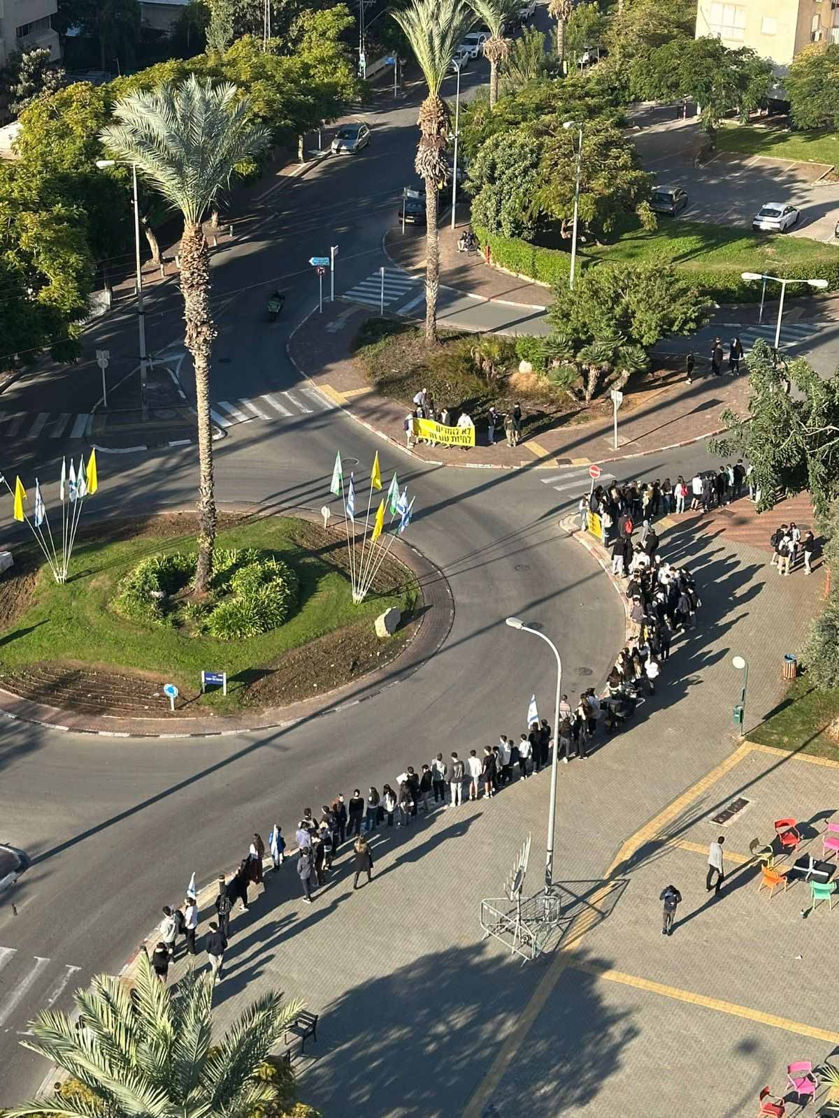 תלמידי גבעתיים מפגינים למען החטופים. צילום אוויר של התלמידים עומדים לאורך המדרכה בכיכר עם דגלים.