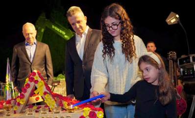 הדלקת נר ראשון בבית הספר שנפגע ברמת אפעל. ילדה קטנה ולידה נערה אוחזות בנר כחול ומדליקות נר ראשון. לצידן עומד ראש העיר רמת גן כרמל שאמה הכהן ושר הביטחון לשעבר יואב גלנט. על שולחן 8 כוסיות עם שמן ופרחים אדומים וצהובים על סמל החטופים.
