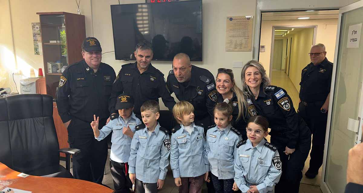 שוטר ליום אחד במשטרת גבעתיים. חמישה ילדים במדי שוטרים ומאחוריהם עומדים חמישה שוטרות ושוטרים. ליד דלת עומד שוטר נוסף.