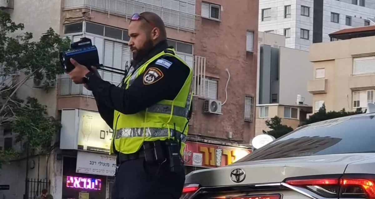 שוטר עם מצלמה ליד ניידת משטרה מצלם כלי רכב.