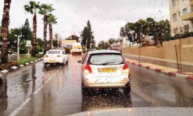 חורף מסוכן ברמת גן וגבעתיים. מכוניות נוסעות בגשם חזק והכביש רטוב. חלון הנהג מלא טיפות גשם.