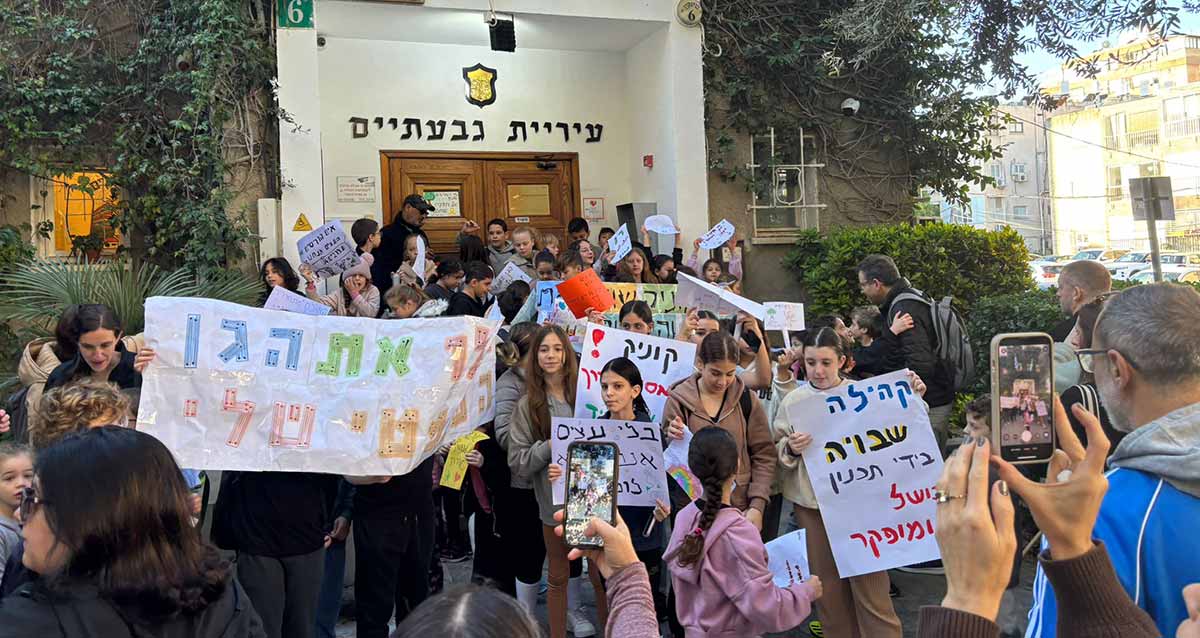 הפגנה נגד עיריית גבעתיים. ילדים עומדים עם שלטים. על שלט קרוב כתוב: קהילה שבויה בידי תכנון כושל ומופקר. ברקע הכניסה לבניין עיריית גבעתיים.