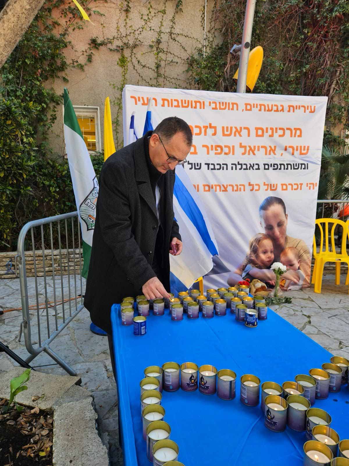 הזדהות עם מסע הלוויה של שירי, אריאל וכפיר. ראש העיר עומד ליד שולחן עם נרות זיכרון ומאחוריו שלט גדול עם התמונות שלהם, דגל המדינה וכיתוב: עיריית גבעתיים, תושבי ותושבות העיר מרכינים ראש לזכרם של שירי, אריאל וכפיר, ומשתתפים באבלה הכבד של המשפחה, יהי זכרם של כל הנרצחים והנופלים ברוך
