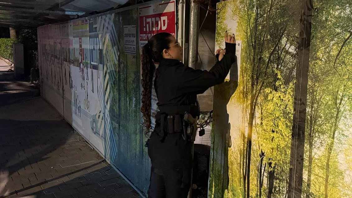 צו סגירה לאתר בנייה ברמת גן. שוטרת מדביקה את הצו עם הקיר המקיף את האתר.
