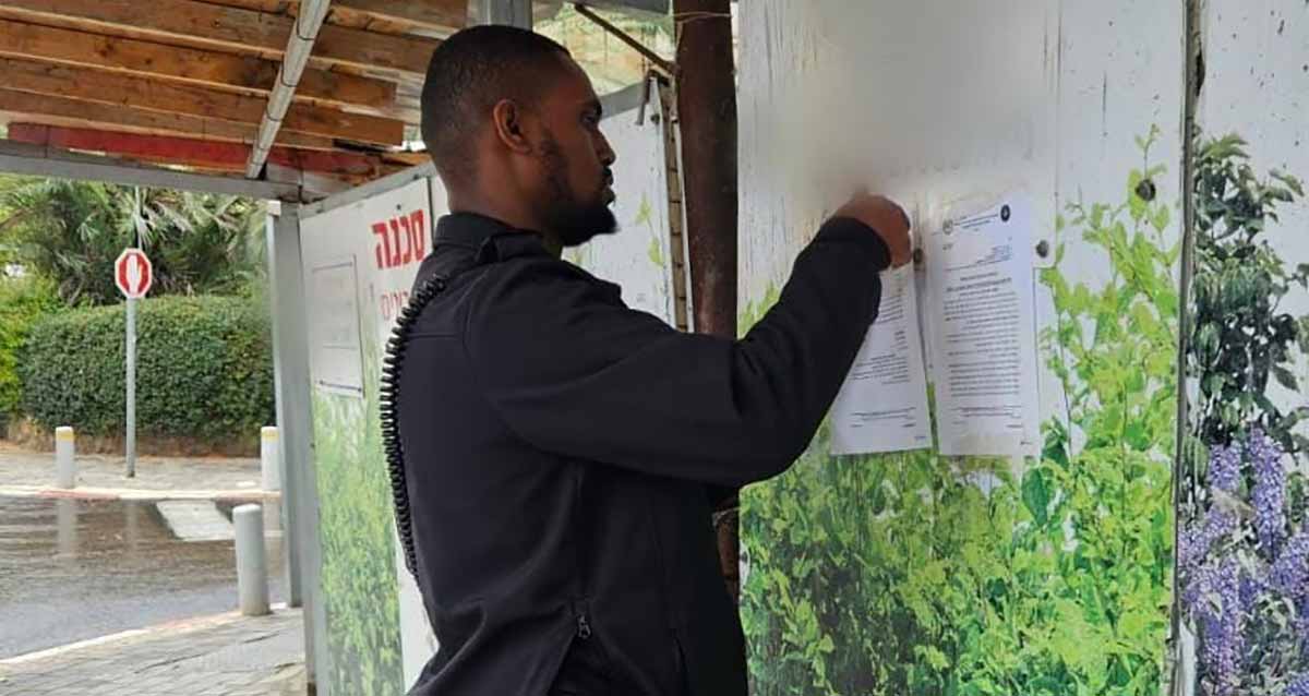 צו סגירה לאתר בנייה ברמת גן שהעסיק שב"ח. שוטר מדביק שני דפים של הצו על קיר אתר הבנייה. משמאלו על הקיר כתוב: סכנה.