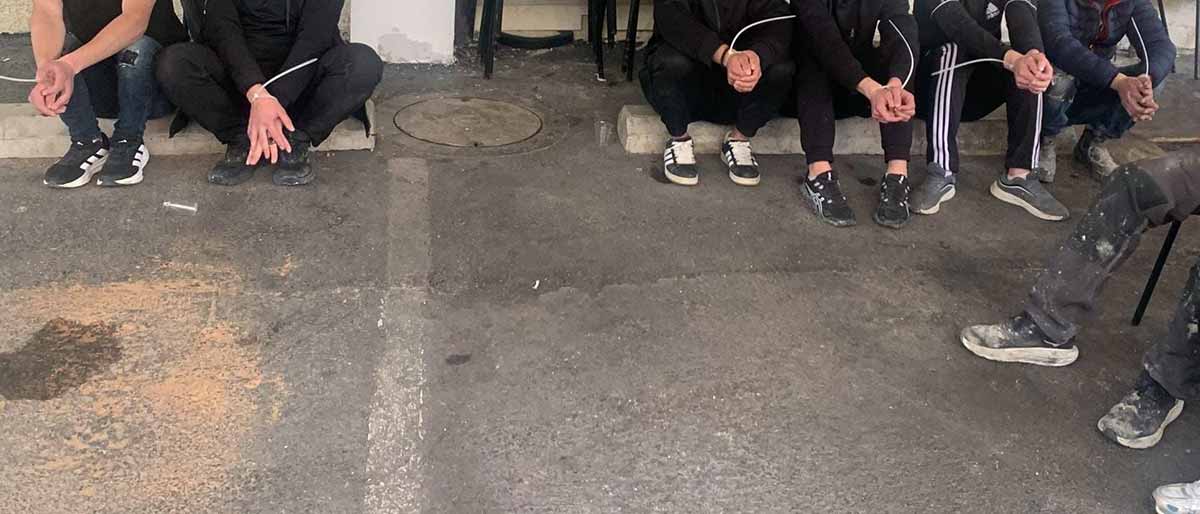 שישה שב"חים נעצרו בעסק בשיפוצים בגבעתיים. השב"חים יושבים עם ידיים אזוקות ובצד ימין יושב שוטר.