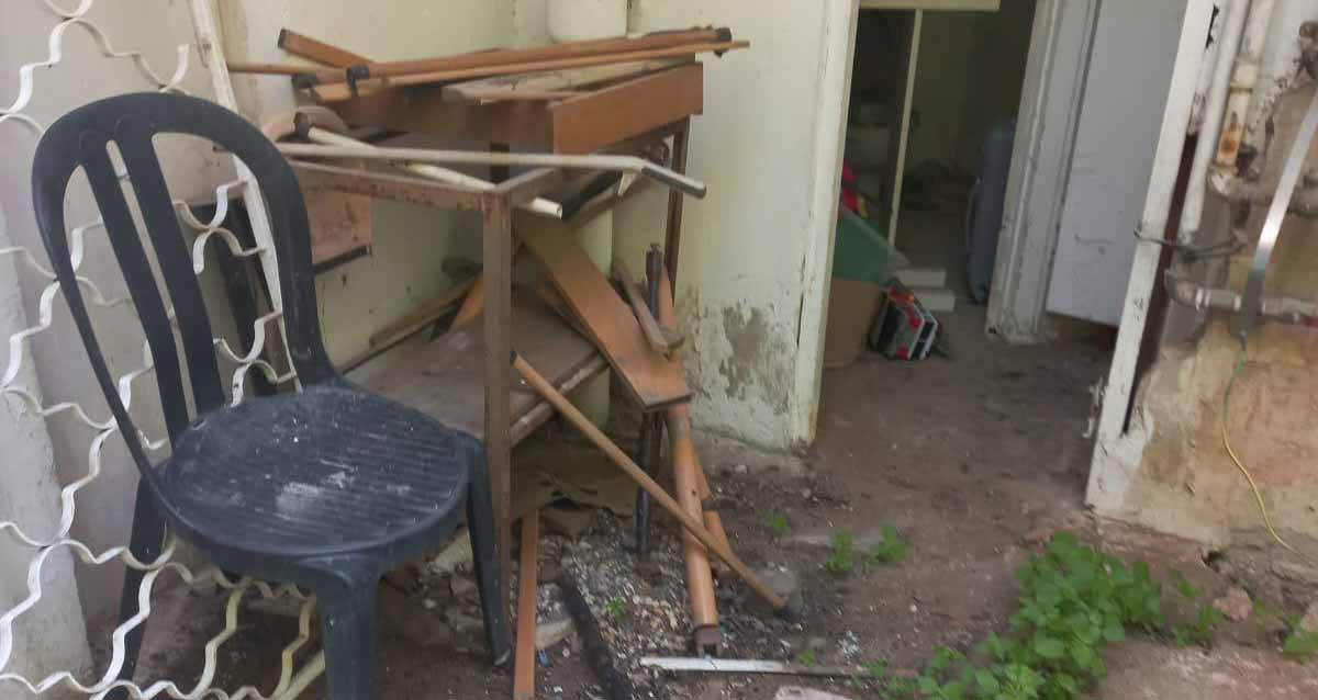הזנחה ברחוב הרא"ה ברמת גן. ליד הכניסה כוננית עם חלקי עץ של ריהוט, ולידה כסא פלסטיק שחור.