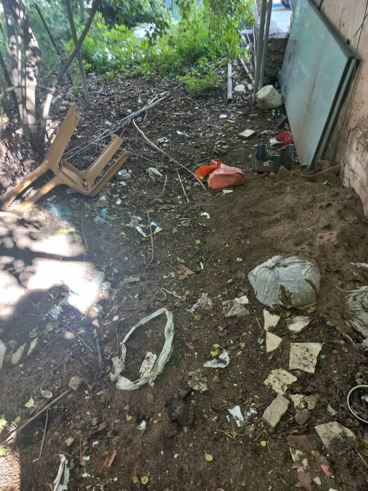 הזנחה ברחוב הרא"ה ברמת גן. אשפה בחצר, שקית עם אשפה, כסא פלסטיק שבור, ודלת הנשענת על הקיר.