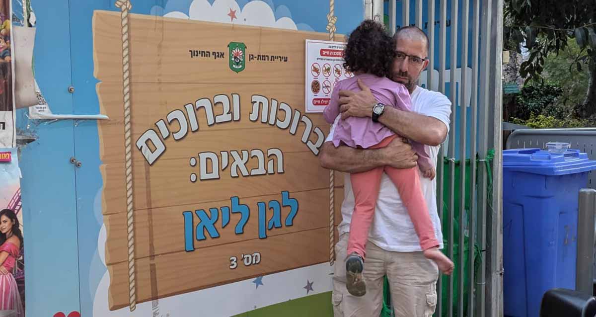 גן ליאן ברמת גן. אבא וילדה בידיים עומד ליד שלט בכניסה לגן. הכיתוב בשלט: ברוכים הבאים: לגן ליאן מס' 3, ובראש השלט כיתוב: עיריית רמת-גן אגף החינוך וסמל העירייה.