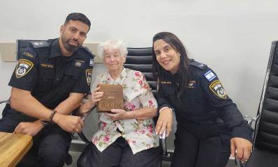 מריאנה לוטן ניצולת שואה יושבת עם ספר תהילים שקיבלה מהשוטרים המלווים אותה. רס"ב הילה אסרף בצד ימין וסנ"צ אליעד אנקרי בצד שמאל.
