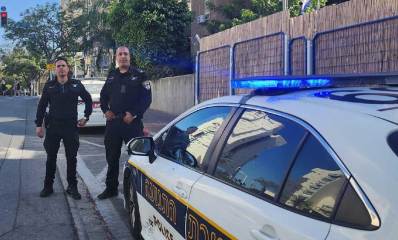 שוטרי תחנת גבעתיים. שני שוטרים לפני ניידת משטרה החונה במקביל למדרכה.