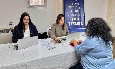 נציבות תלונות הציבור במשרד מבקר המדינה תגיע לרמת גן. שתי עובדות של מבקר המדינה יושבות עם מחשבים ניידים ומולן יושבת אישה. מאחוריהן שלט עם הכיתוב: נציבות תלונות הציבור במשרד מבקר המדינה כאן בשבילך.