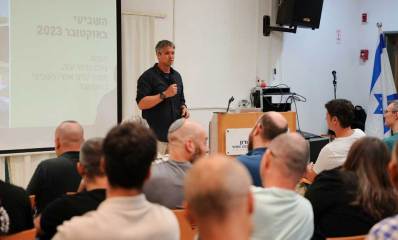 יועז הנדל בהקמת מטה תנועת "המילואימניקים" בבית דורון. יושבים בשורות מול דוכן נואמים שמאחוריה עומד יועז הנדל ולפניו מיקרופון.