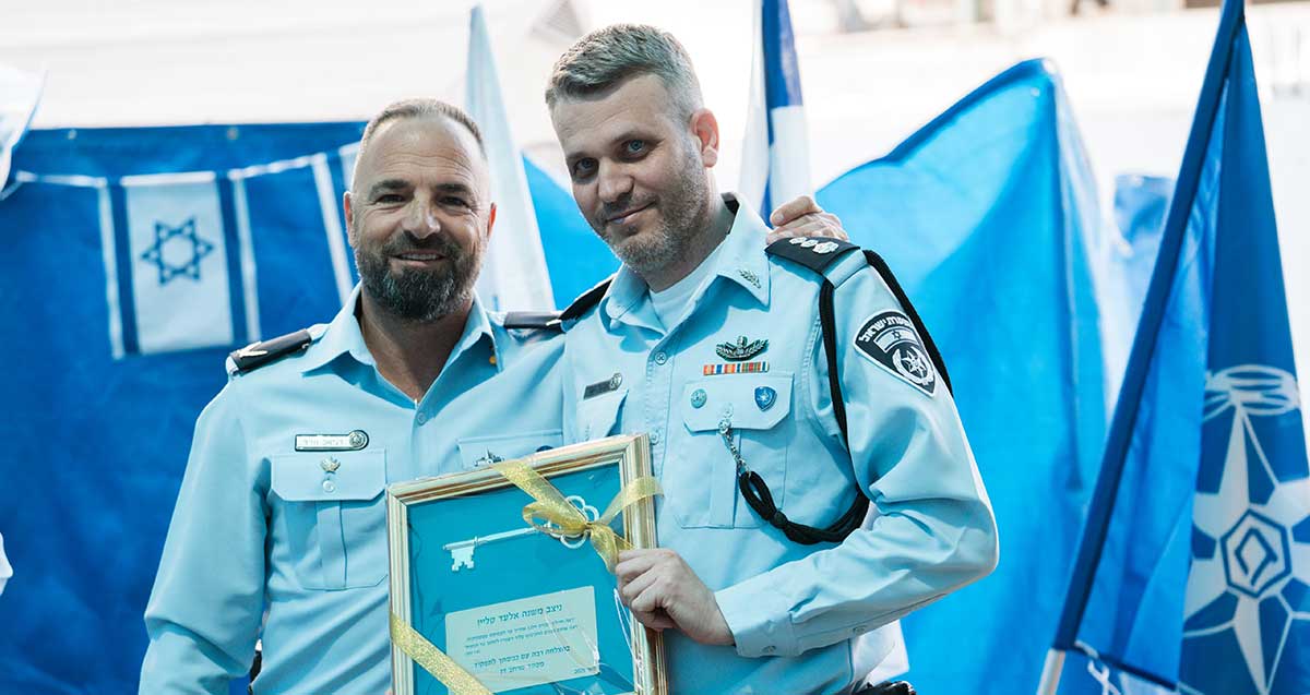 נצ"מ אלעד קליין מפקד מרחב דן אוחז תעודה ממוסגרת ולידו קצין משטרה. מאחוריהם דגלים.