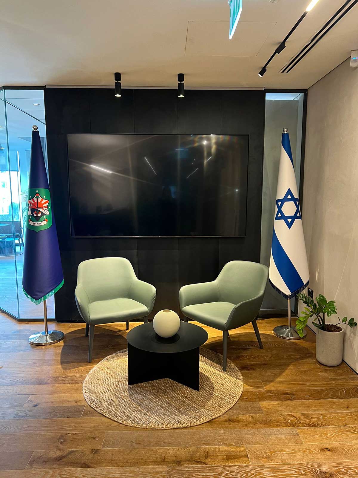 לשכת ראש עיריית רמת גן במגדל ספיר. שתי כורסאות ושולחן עגול. דגל המדינה מימין ודגל העיר משמאל. מאחורי הכורסאות מסך ענק.