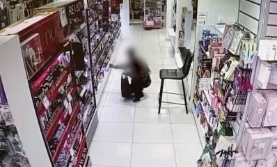 גנב הבשמים שנתפס בגבעתיים עם תיק שחור מתכופף ליד מדפי הבשמים. פניו מטושטשות.