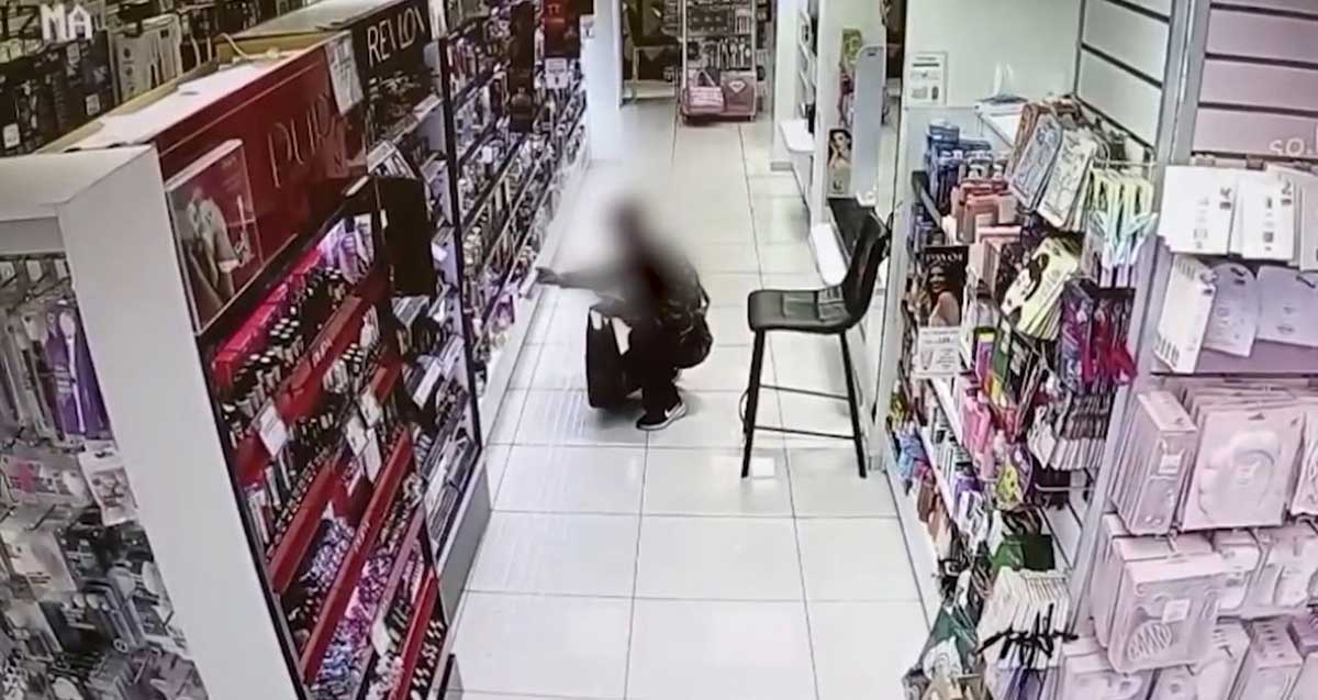 גנב הבשמים שנתפס בגבעתיים עם תיק שחור מתכופף ליד מדפי הבשמים. פניו מטושטשות.