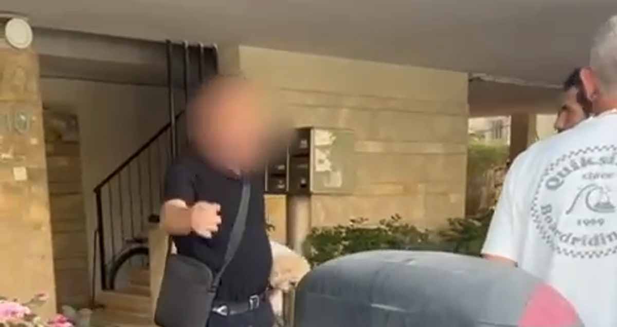 אדם עם טשטוש על הפנים וכלב ביד עומד בלובי כניסה לבניין ומונע כניסת שני דרוזים למקלט של בניין בעת אזעקה.