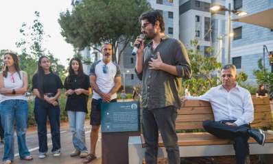 רן דנקר במחווה למשפחה מרמת גן עומד עם מיקרופון ביד. לידו יושב על ספסל ראש העיר. וקהל בצד.