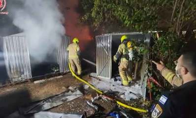 שריפה במחסן ברחוב הרא"ה ברמת גן. שני כבאים עם זרנוק ליד המחסן. שוטר עומד בקרבת מקום.