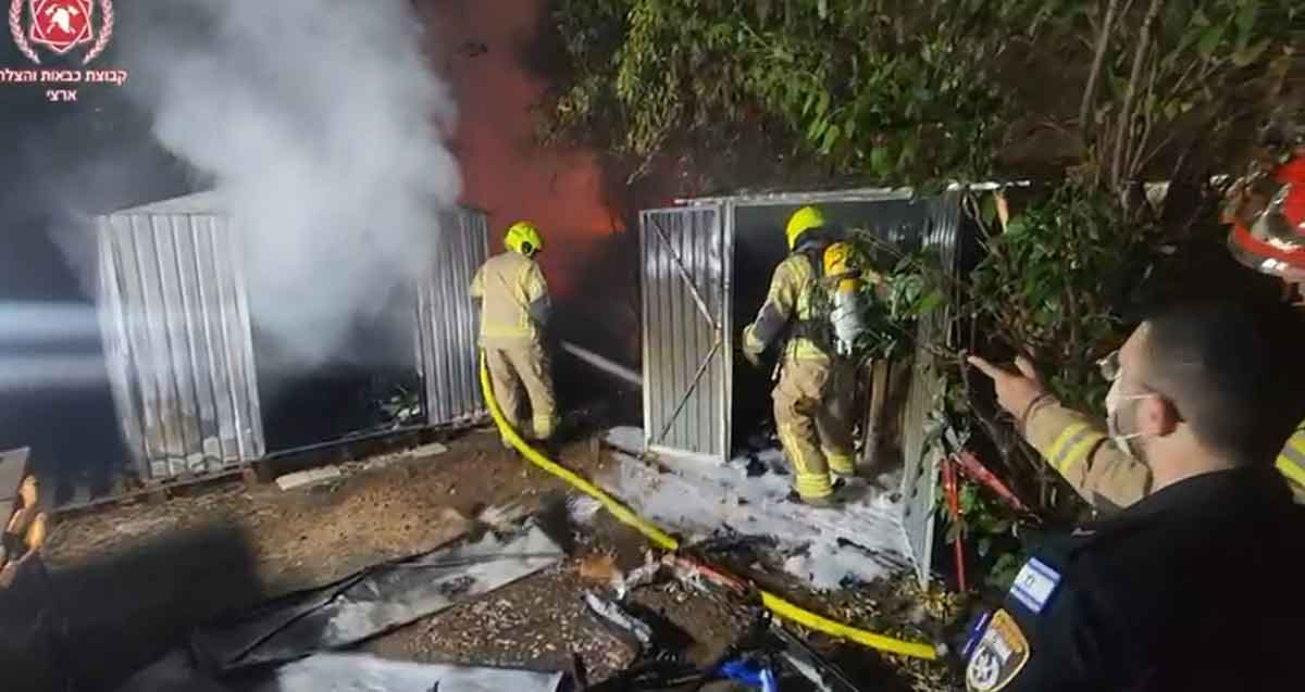 שריפה במחסן ברחוב הרא"ה ברמת גן. שני כבאים עם זרנוק ליד המחסן. שוטר עומד בקרבת מקום.