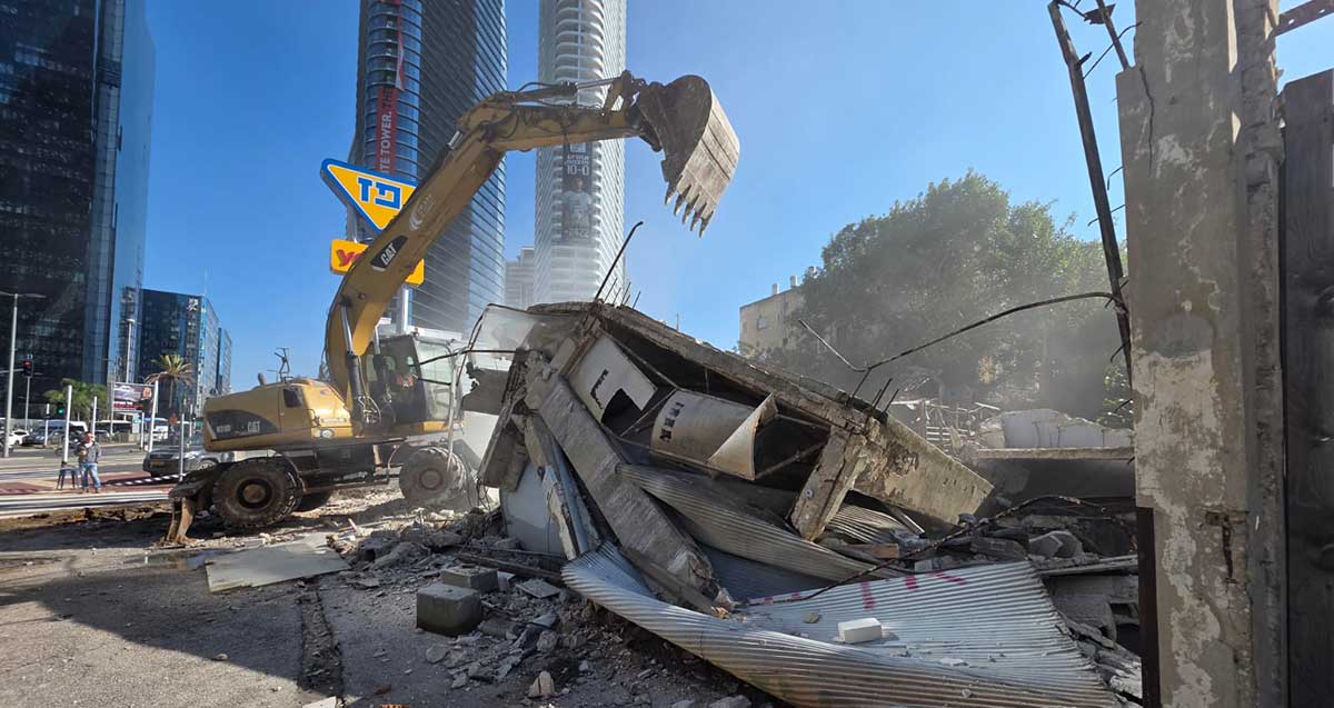 טרקטור הורס מבנה ישן בצומת עלית. ברקע מגדלים